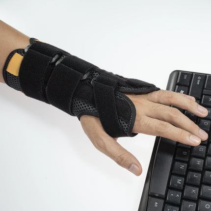 Hand wearing a black wrist support brace using a keyboard on a white background
