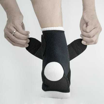 Person wearing a black ankle support brace on a plain background